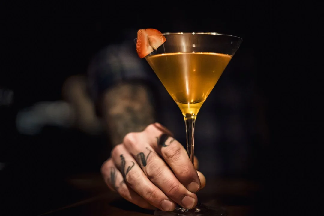 Elegant interior of Galt House Jockey Silks bar with black leather couches, round chairs, a central table with wine, and a well-stocked bar in the background. Warm lighting creates a sophisticated atmosphere.