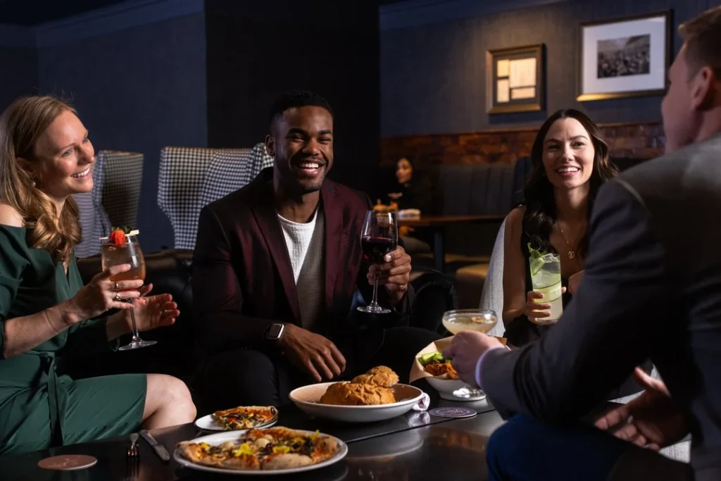 Four adults sit around a table in a restaurant, enjoying drinks and food. They are laughing and talking, creating a lively, social atmosphere.